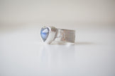 A sterling silver ring featuring a heart shaped labradorite gemstone with a bright blue flash. The band is hand sawed with an EKG heart rhythm. 