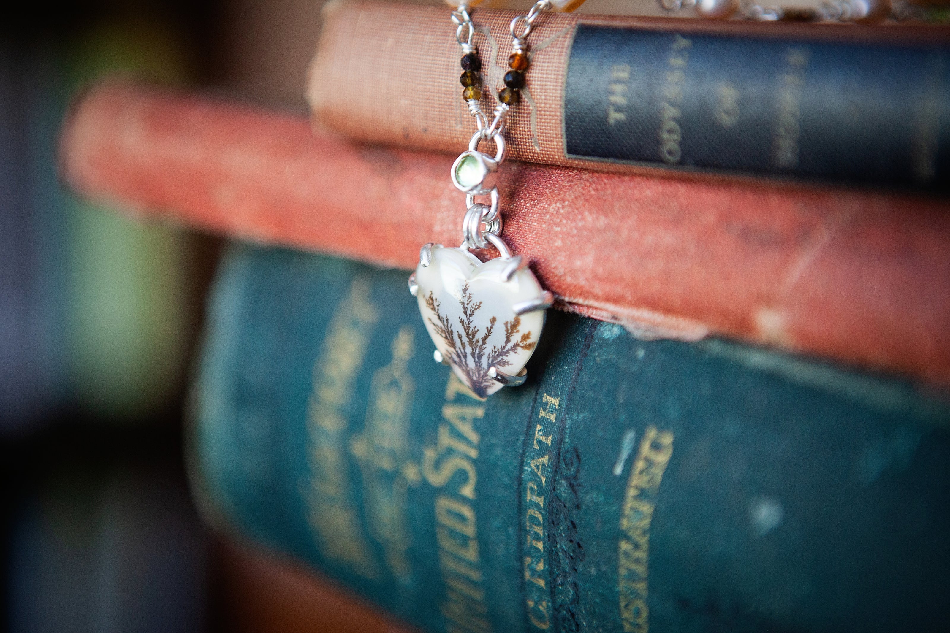 A necklace with a handmade sterling silver pendant featuring a heart shaped dendritic agate and a tiny peridot gemstone. The chain is made from tourmaline, pearl, and peridot beads. 