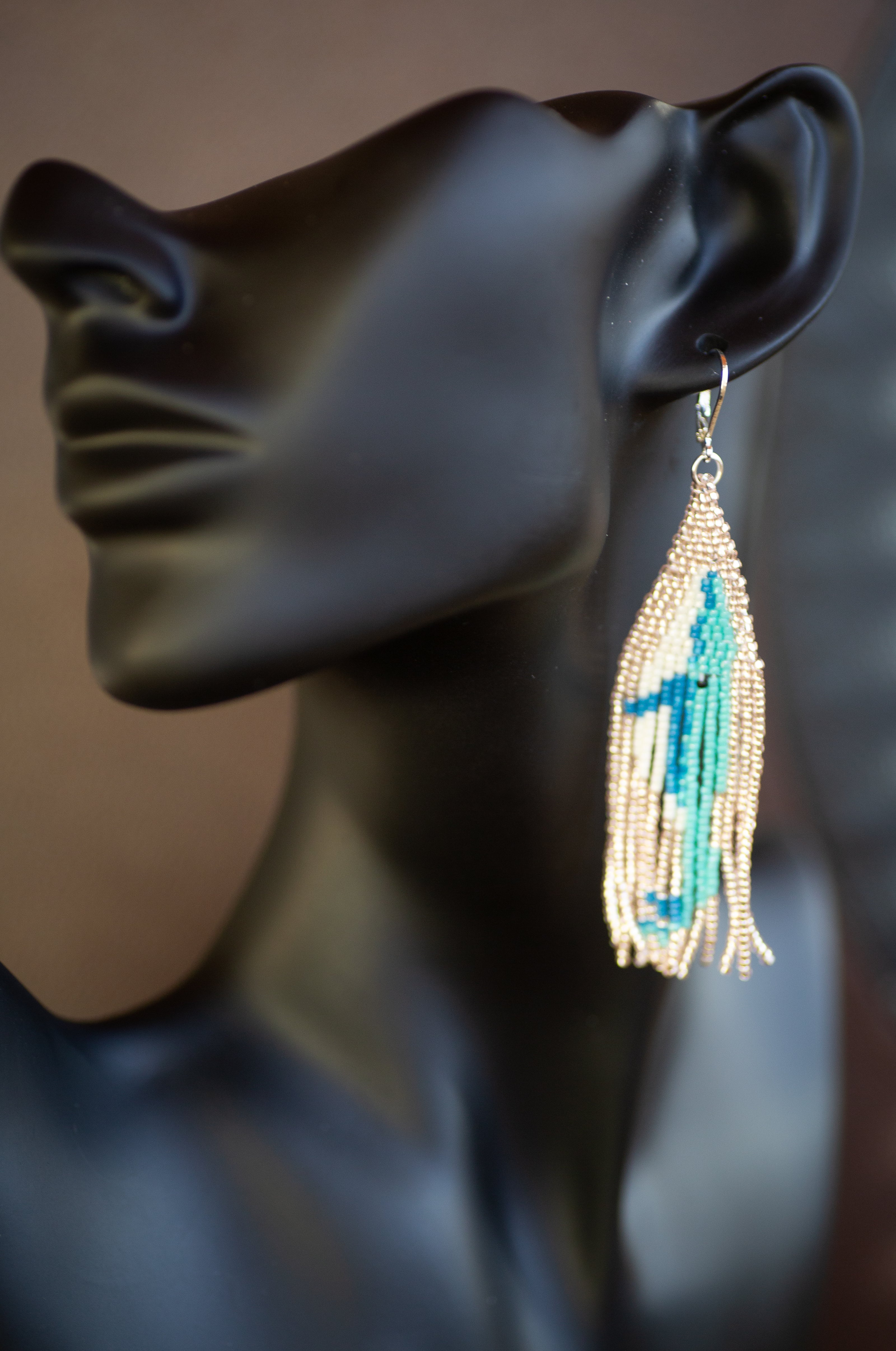 Beaded tassel earring on a mannequin ear with a blurred background