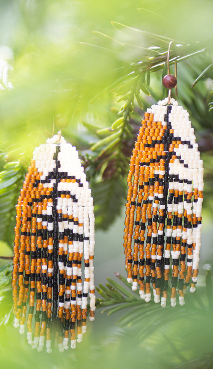 Beaded earrings that look like Red Tailed Hawk feathers hanging on a branch with green leaves in the background