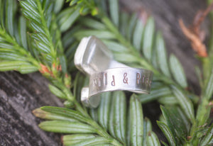 Silver ring with engraved text on a bed of green leaves. Inscribed with the words wild and precious. 