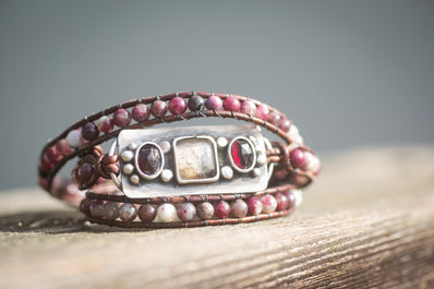 An adjustable leather wrap bracelet with sterling silver, dendritic agate, and garnet gemstones. 