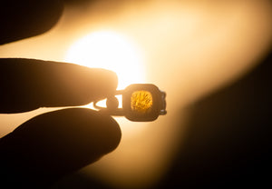 A sterling silver dendritic agate ring, held up to a warm light source to reveal the natural pattern of the agate. 