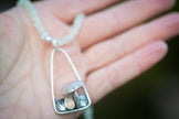 Silver necklace with a pendant shaped like a mushroom held in a hand.