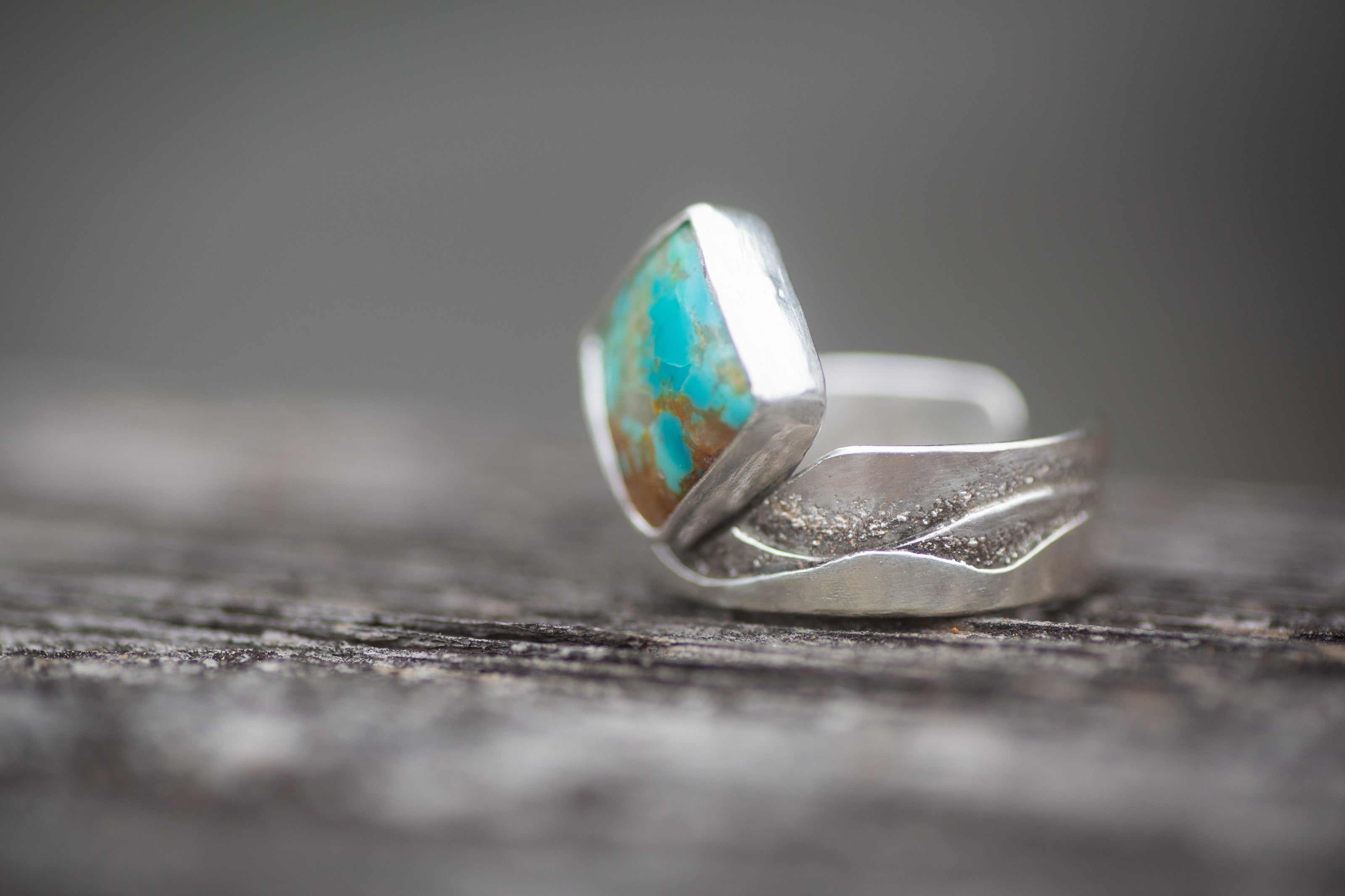 This turquoise and sterling silver ring has a textured band with a wave or mountain pattern. 