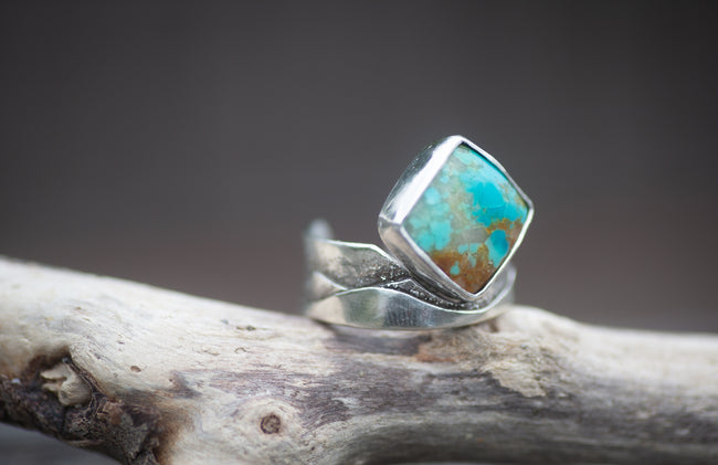 A ring featuring a diamond shaped turquoise stone with a textured sterling silver band. 