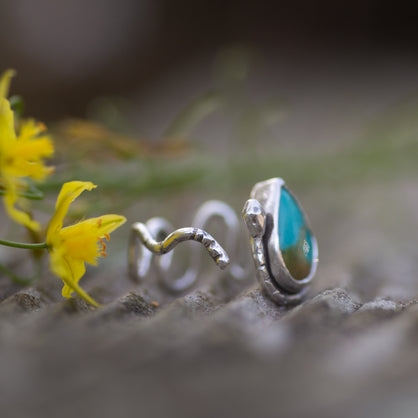 A sterling silver ring with teal turquoise stone. The ring is shaped like a rattlesnake.