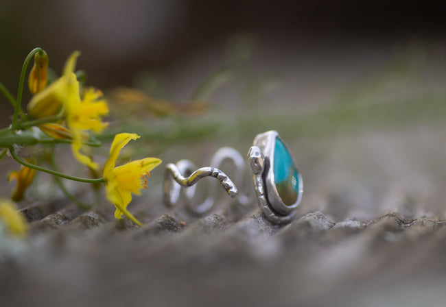 A sterling silver ring with teal turquoise stone. The ring is shaped like a rattlesnake.